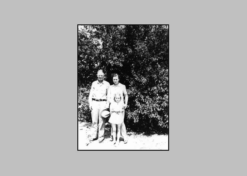 Adron, holding his hat in his hand, Johnie and Adrienne standing in front of some trees