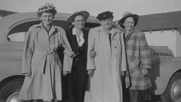 <aunts carl, lizzie, tudy and bug standing in front of aunt lizzie's chevy car at house, nm>